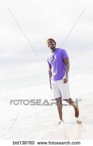 Stock Image - Mixed race man walking on beach. Fotosearch