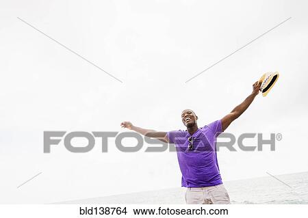 Picture - Mixed race man with arms outstretched on beach. Fotosearch