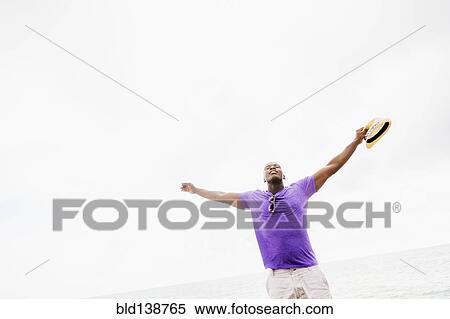 Stock Photography - Mixed race man with arms outstretched on beach. Fotosearch