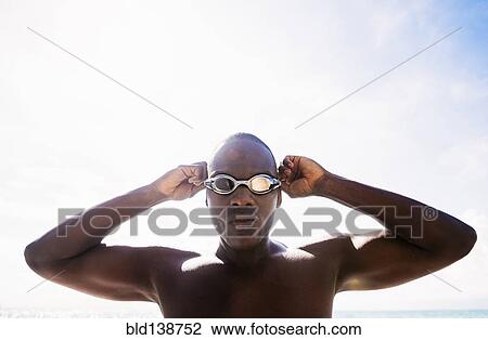 Stock Image - Mixed race swimmer putting on goggles. Fotosearch