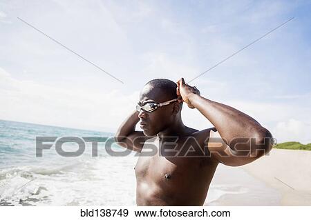 Stock Photo - Mixed race swimmer putting on goggles at beach. Fotosearch