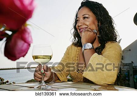 Stock Image - Mixed race woman drinking wine at waterfront. Fotosearch