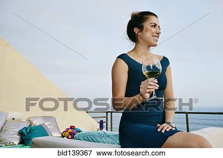 Stock Photo - Mixed race woman drinking wine at waterfront. Fotosearch