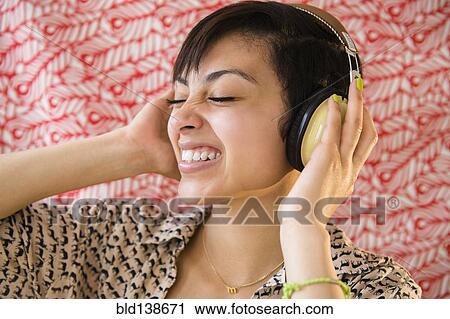 Stock Image - Mixed race woman listening to headphones. Fotosearch