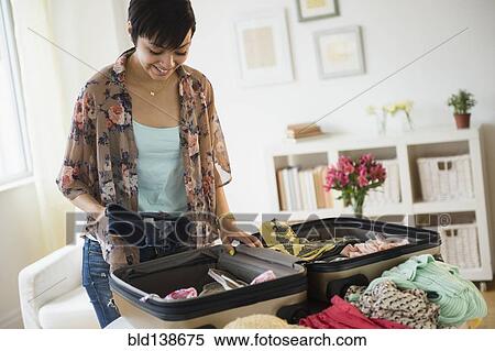 Stock Photography - Mixed race woman packing suitcase for vacation. Fotosearch