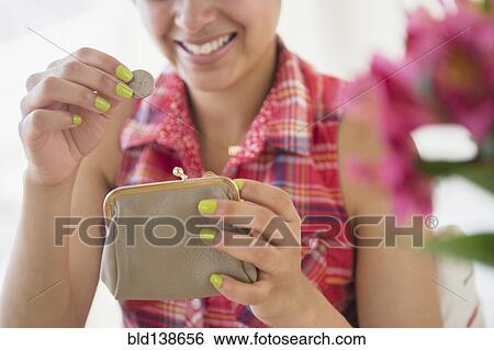 Stock Photograph - Mixed race woman putting coin into purse. Fotosearch
