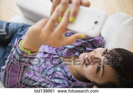 Stock Image - Mixed race woman taking selfie with cell phone. Fotosearch