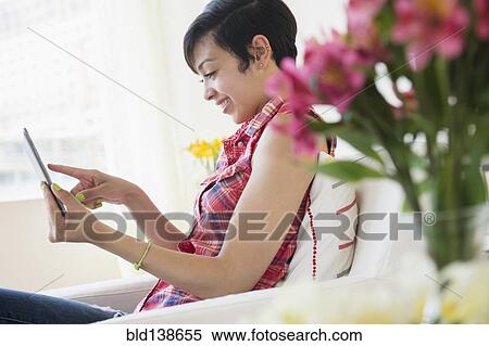 Stock Photography - Mixed race woman using digital tablet on sofa. Fotosearch