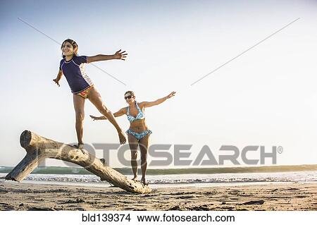 Picture - Mother and daughter playing on log on beach. Fotosearch