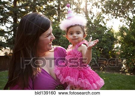 Mother holding daughter in party hat in backyard View Large Photo Image Stock Image - Mother holding daughter in party hat in backyard. Fotosearch