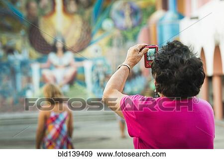 Older woman photographing urban mural View Large Photo Image Stock Photo - Older woman photographing urban mural. Fotosearch
