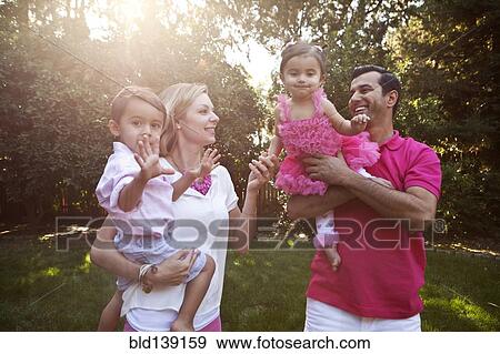 Stock Photo - Parents holding children together in backyard. Fotosearch