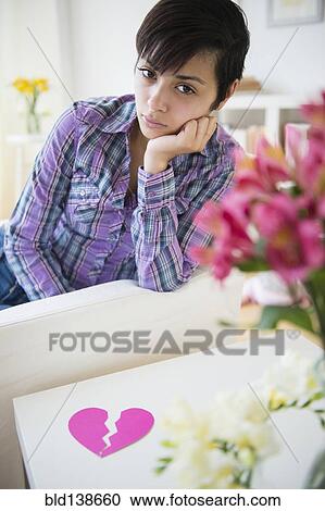 Stock Image - Sad mixed race woman on sofa with broken heart. Fotosearch