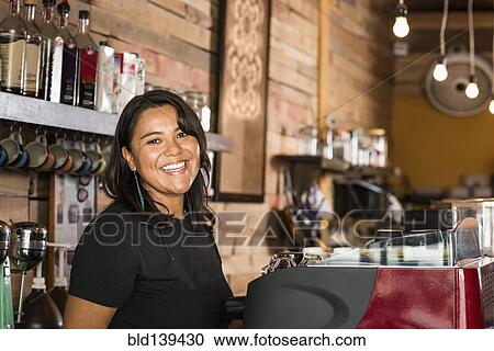 Stock Image - Smiling Hispanic woman working in coffee shop. Fotosearch