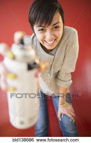Stock Photograph - Smiling mixed race woman holding canister of spray paint. Fotosearch