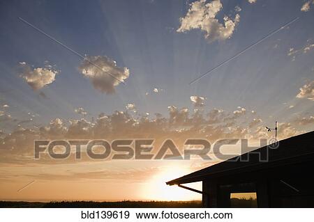 Stock Photo - Sunbeams through clouds over house. Fotosearch