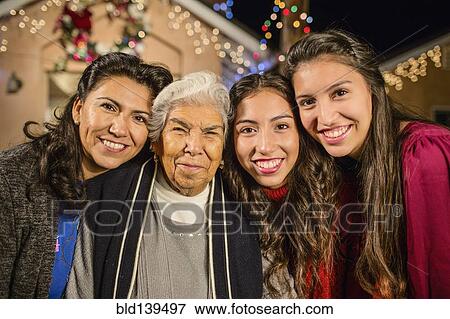 Three generations of Hispanic women standing outside house decorated with string lights View Large Photo Image Stock Photo - Three generations of Hispanic women standing outside house decorated with string lights. Fotosearch