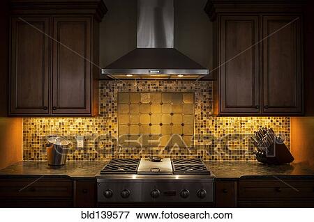 Stock Photo - Tile back splash, ventilation hood and stove in dark kitchen. Fotosearch