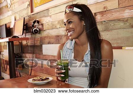 Stock Image - African American woman having juice in cafe. Fotosearch