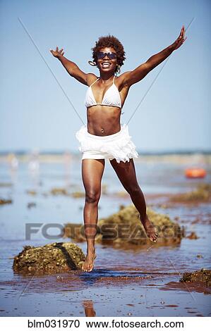 Stock Image - Black woman playing on rocky beach. Fotosearch