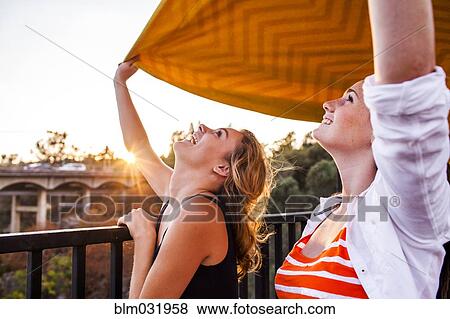 Stock Photo - Caucasian teenage girls holding blanket on bridge. Fotosearch
