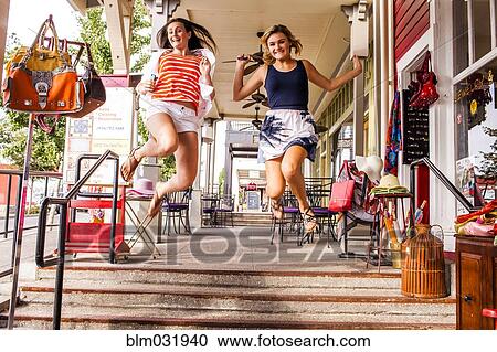Stock Image - Caucasian teenage girls jumping for joy in city. Fotosearch