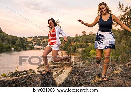 Stock Image - Caucasian teenage girls running on riverbank. Fotosearch