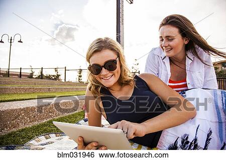 Stock Photograph - Caucasian teenage girls using tablet computer in park. Fotosearch