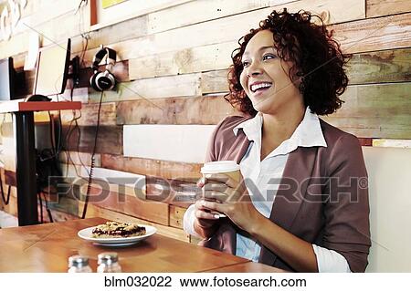 Stock Image - Mixed race businesswoman having coffee and pastry in cafe. Fotosearch