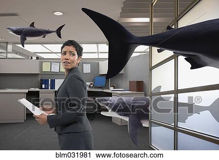 Stock Image - Mixed race businesswoman watching shark in office. Fotosearch