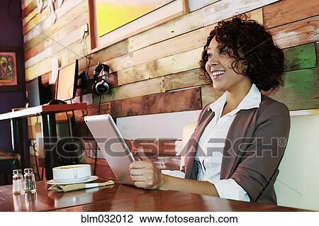 Stock Image - Mixed race woman using tablet computer in cafe. Fotosearch