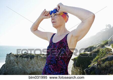 Stock Photography - Older Caucasian woman putting on goggles on beach. Fotosearch