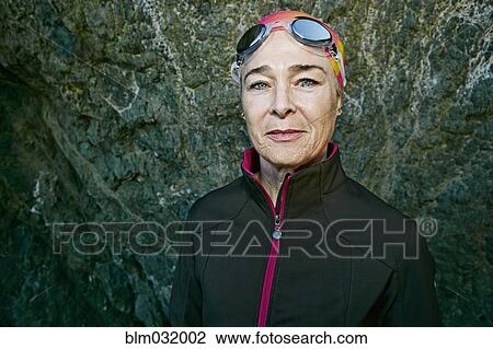 Stock Image - Older Caucasian woman wearing goggles near rock. Fotosearch