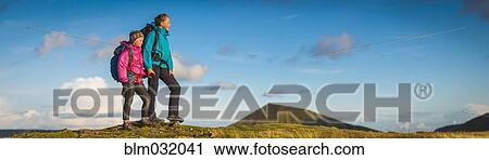 Panoramic view of hikers walking up grassy hill View Large Photo Image Stock Image - Panoramic view of hikers walking up grassy hill. Fotosearch