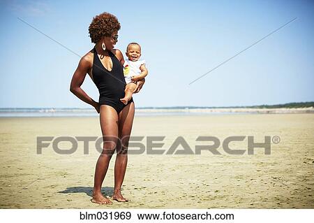 Stock Photo - Smiling mother holding girl on beach. Fotosearch