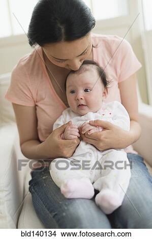 Picture - Asian mother holding baby in armchair. Fotosearch