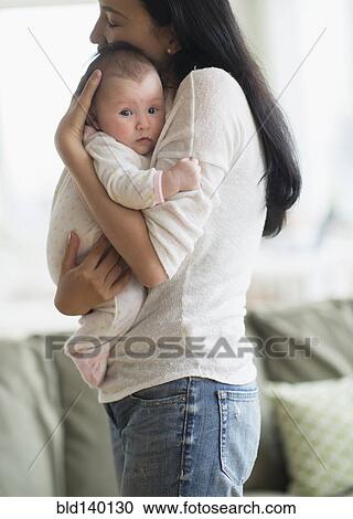 Stock Image - Asian mother holding baby in living room. Fotosearch