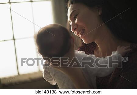 Asian mother holding baby near window View Large Photo Image Stock Photo - Asian mother holding baby near window. Fotosearch