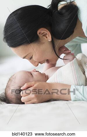 Stock Image - Asian mother holding baby on bed. Fotosearch