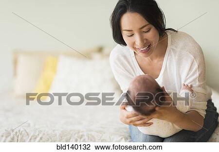 Asian mother holding baby on bed View Large Photo Image Stock Image - Asian mother holding baby on bed. Fotosearch
