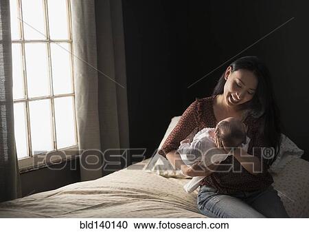 Stock Image - Asian mother holding baby on bed. Fotosearch