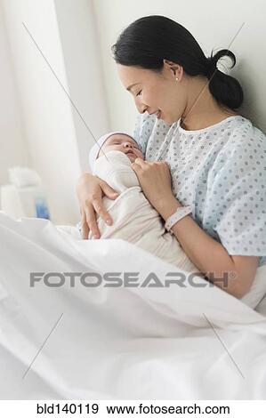 Asian mother holding newborn baby in hospital bed View Large Photo Image Stock Photo - Asian mother holding newborn baby in hospital bed. Fotosearch