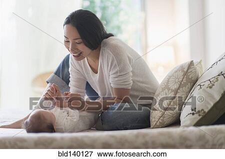 Stock Photo - Asian mother playing with baby on bed. Fotosearch