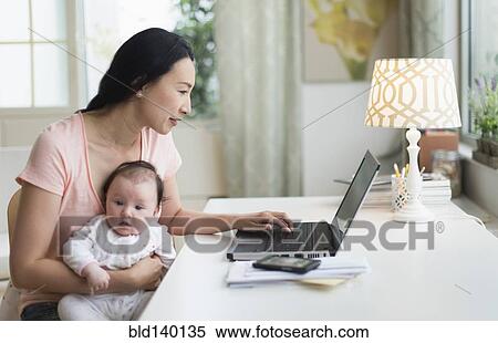 Stock Photography - Asian mother with baby working from home. Fotosearch