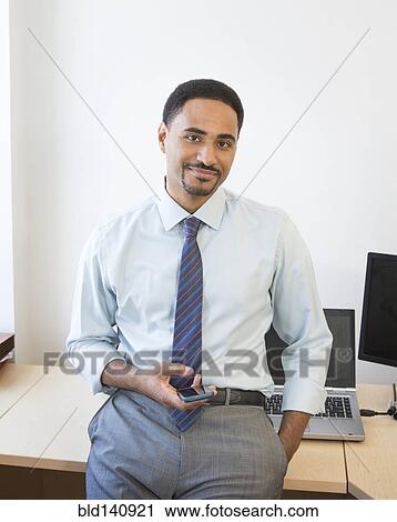 Black businessman holding cell phone in office View Large Photo Image Stock Image - Black businessman holding cell phone in office. Fotosearch