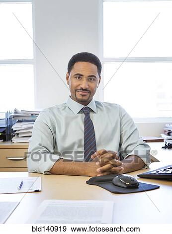 Black businessman sitting at desk View Large Photo Image Stock Photo - Black businessman sitting at desk. Fotosearch