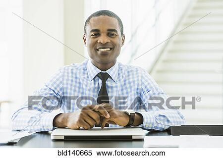 Stock Photography - Black businessman smiling at desk in office. Fotosearch