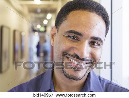 Stock Photo - Black businessman smiling in office hallway. Fotosearch