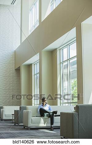 Stock Photograph - Black businessman talking on cell phone in office lobby. Fotosearch