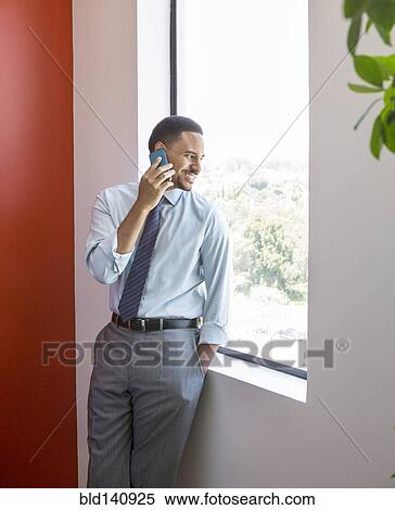 Stock Photography - Black businessman talking on cell phone at office window. Fotosearch